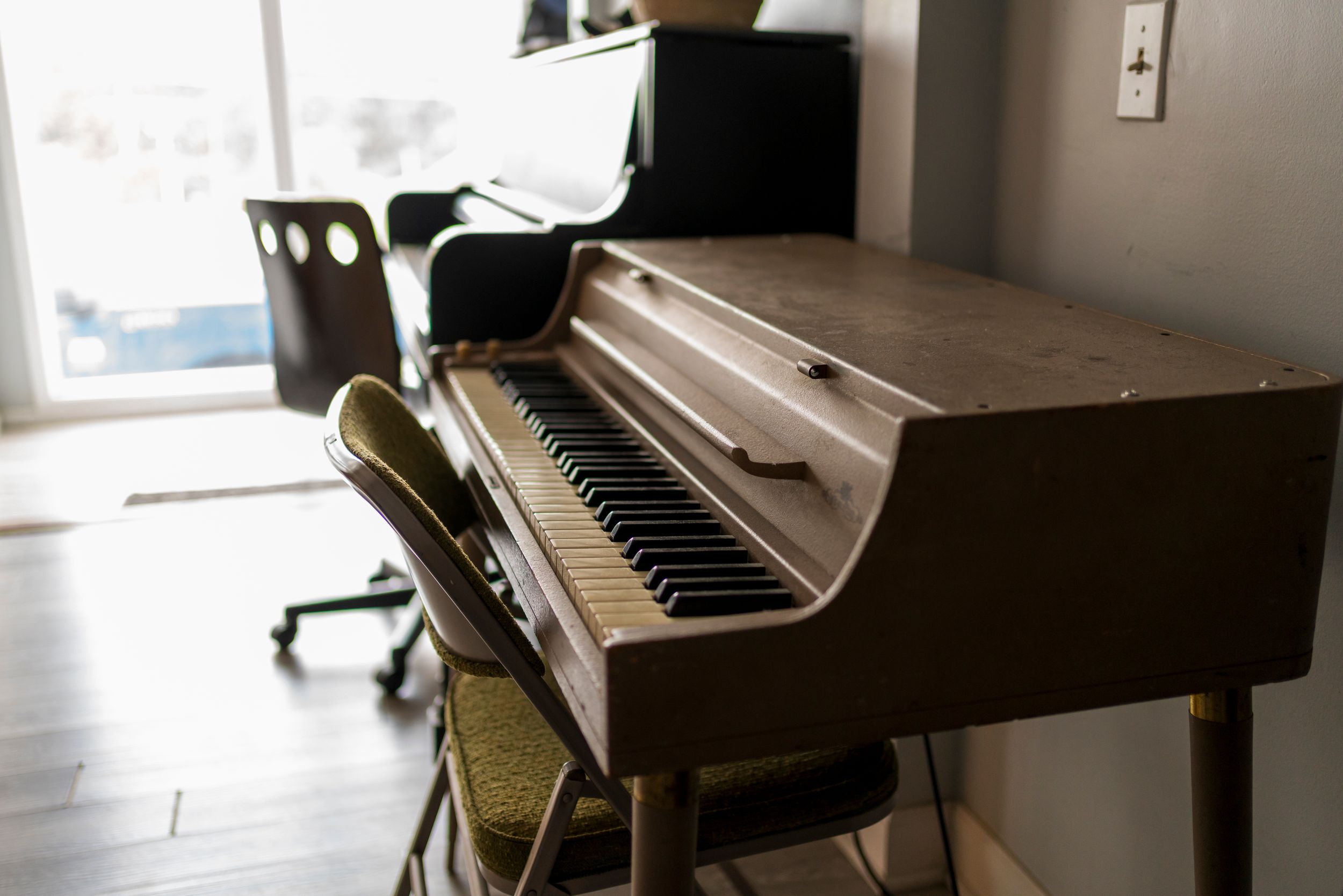 A row of upright pianos in a music studio with natural light streaming through the windows.