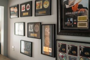 A wall gallery displaying framed gold and platinum record awards and music memorabilia in black frames.