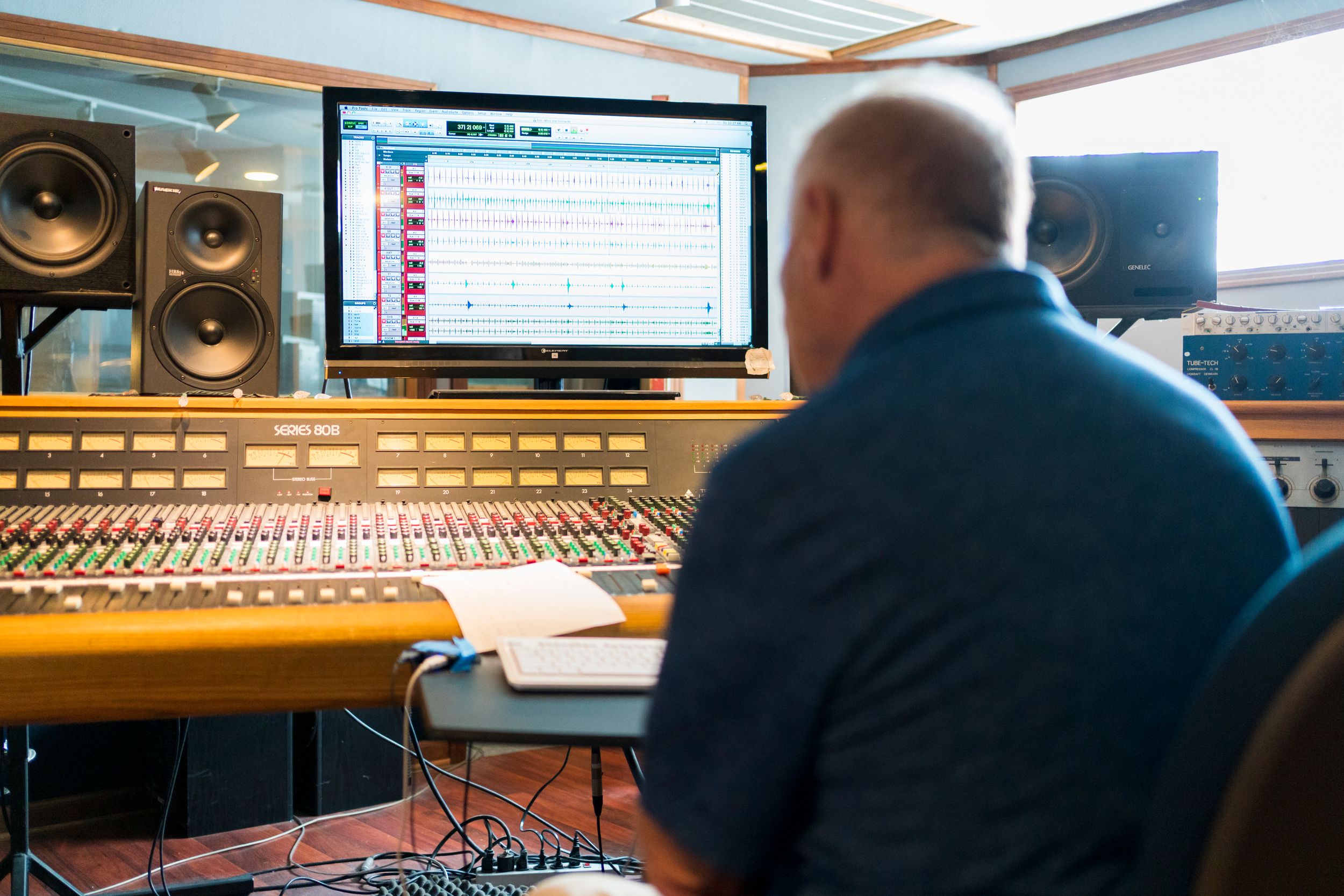 Sound engineer working at mixing console in professional recording studio with computer monitor displays.