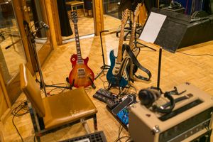 Music studio setup featuring various musical instruments including guitars and audio equipment on wooden flooring in warm lighting.
