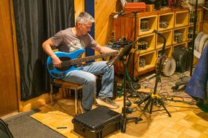 A recording studio with warm wood paneling showing multiple angles of a drummer performing at an acoustic drum kit.