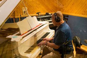Musician playing keyboard in recording studio with wooden floors and warm ambient lighting.