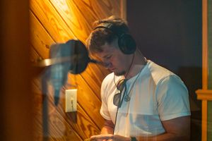 Recording artist wearing headphones in a warmly lit studio booth.