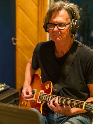 Musician playing electric guitar while wearing headphones in recording studio.