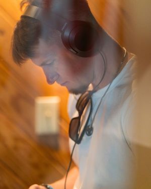 Person in white shirt wearing headphones in recording studio with warm lighting.