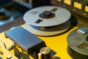 Professional audio reel-to-reel tape recorder with metal reels on yellow surface.