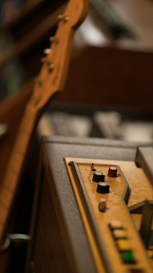 Close-up shot of wooden guitar neck and control knobs on an amplifier in shallow focus.