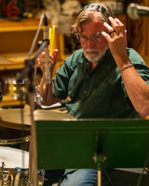 Drummer with glasses focuses intently while performing with drumsticks behind a drum kit.