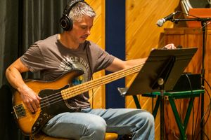 Bass player reads sheet music while performing in a recording studio with headphones.