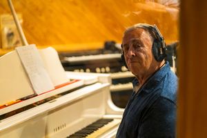 Piano player wearing headphones sits at white Yamaha piano in recording studio.
