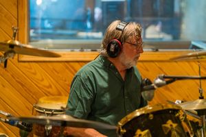 Musician wearing headphones while playing drums in professional recording studio setting.