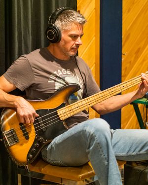 Musician playing an orange bass guitar while wearing headphones in a recording studio.