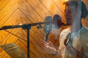 A vocalist performing into a professional studio microphone with dramatic lighting against wood paneled walls.