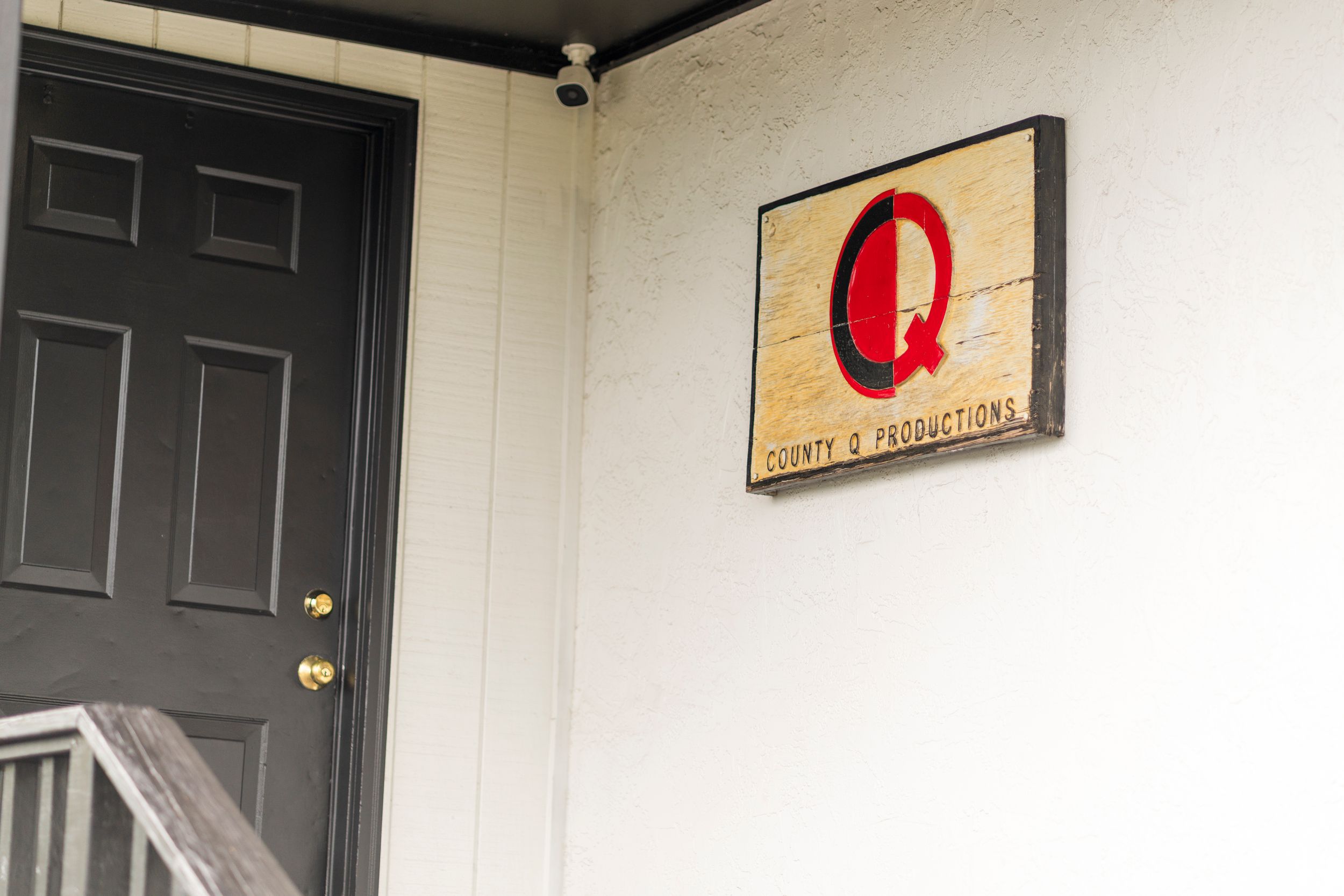 Large red Q sign mounted on white wall next to dark door.