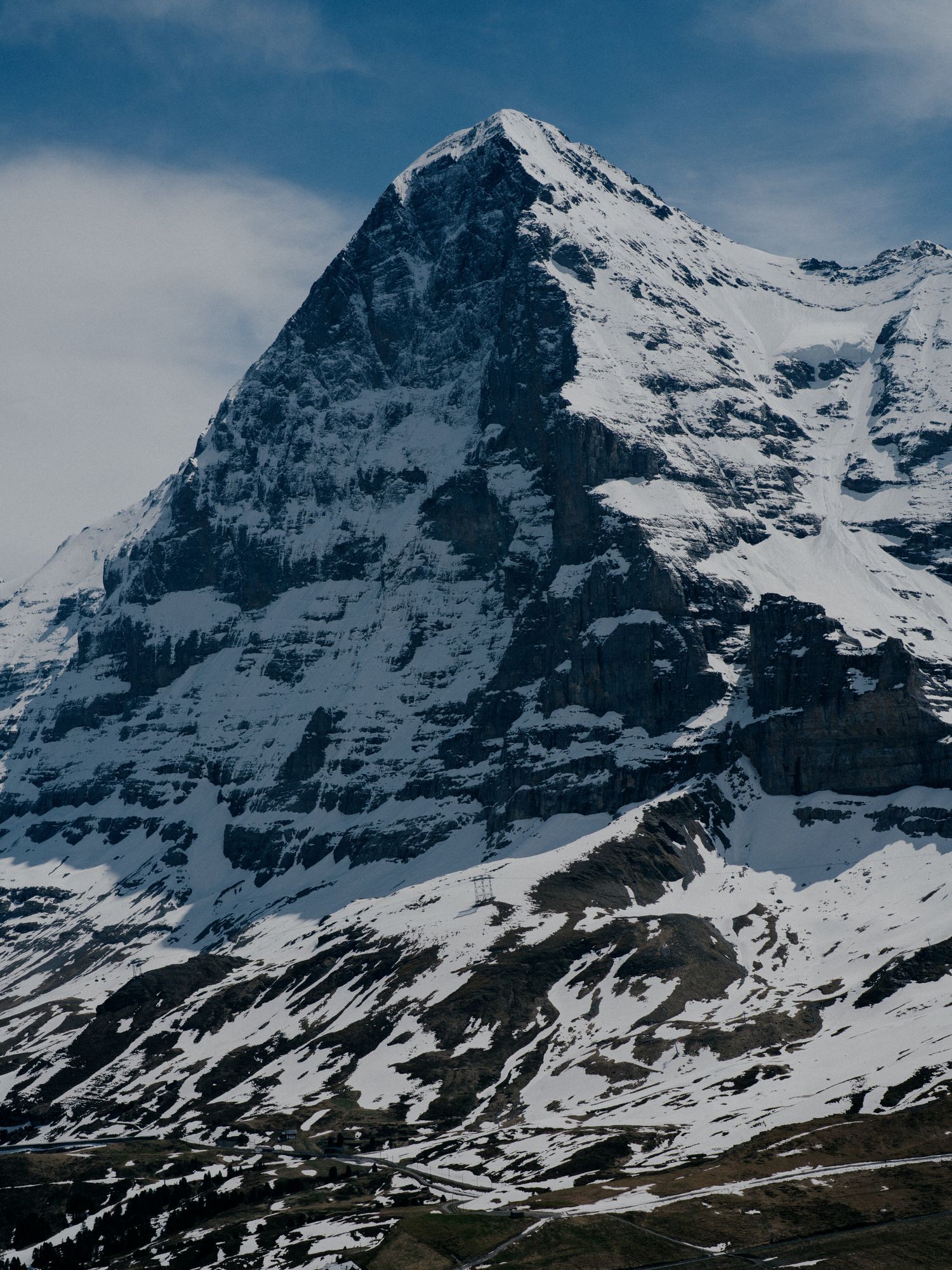 Snow-covered rocky peak of the Eiger mountain in Switzerland towers against a blue sky with dramatic shadows and terrain.