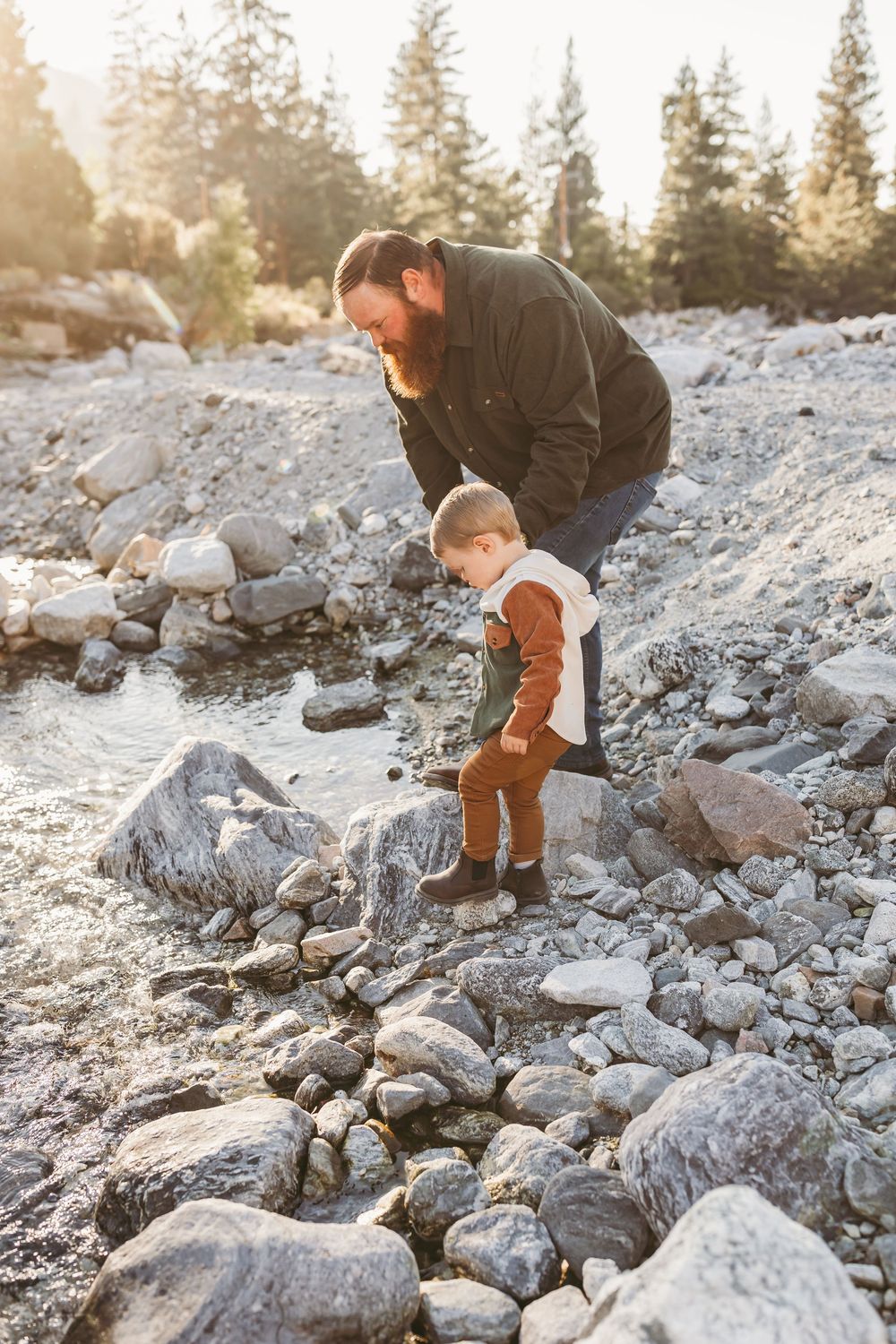 Two people exploring a rocky riverbed together on a sunny day in the forest.