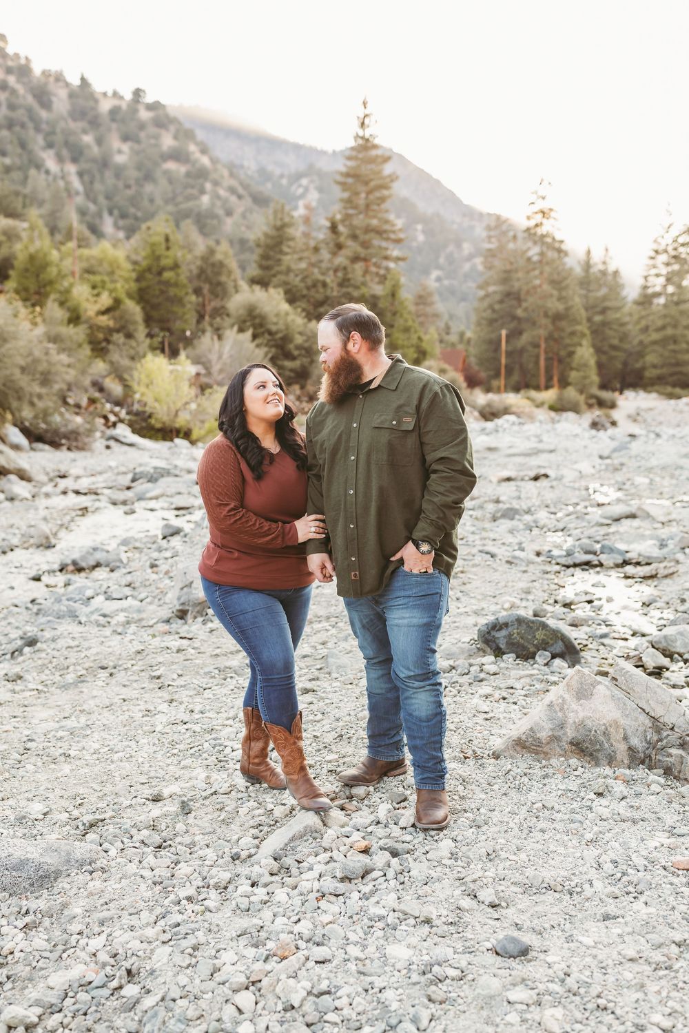 Couple in casual fall attire sharing a romantic moment on rocky mountain terrain surrounded by evergreen trees.