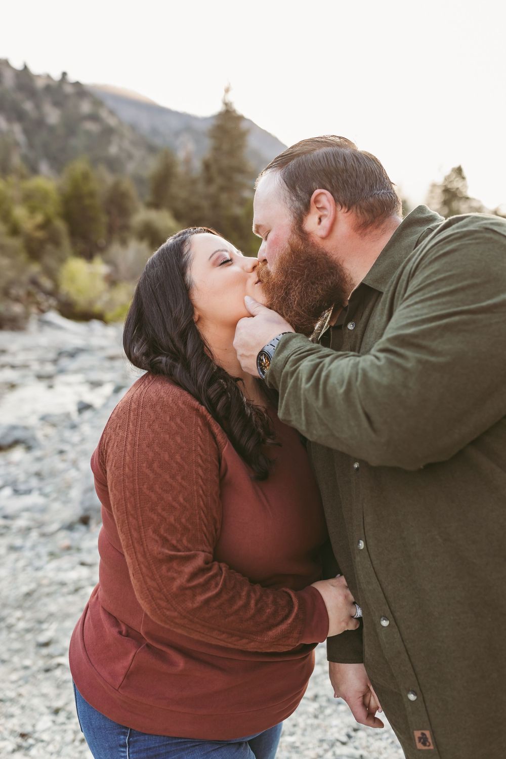 A couple in cozy sweaters sharing an intimate moment on a rocky mountain trail.