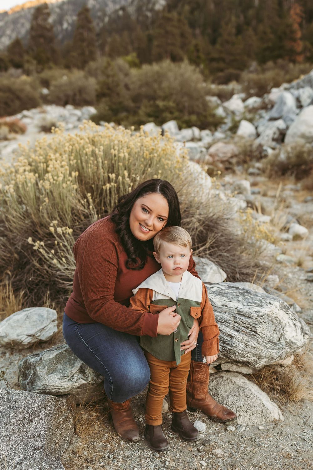 A family poses together on rocky terrain with sage brush during golden hour in the mountains.