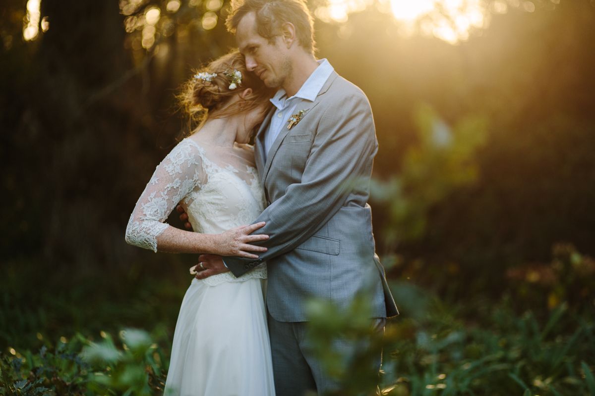 A couple embraces during a romantic sunset wedding photoshoot in a natural outdoor setting among foliage.