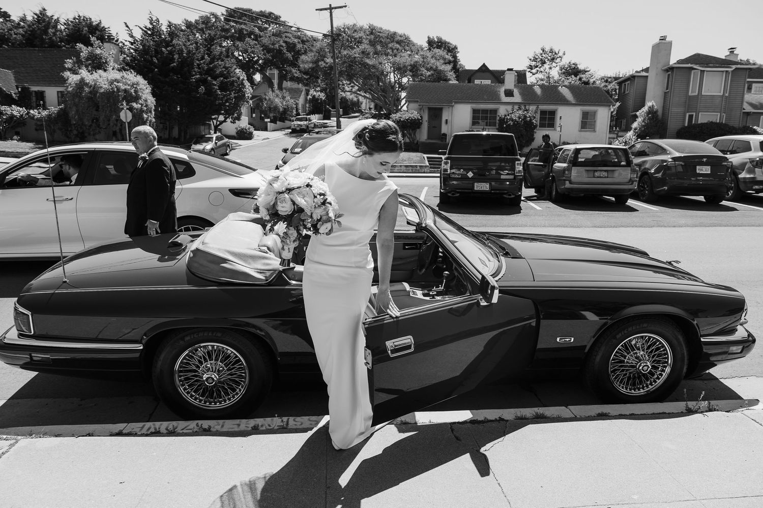 A classic convertible Jaguar XK parked on a sunny residential street in black and white photography.