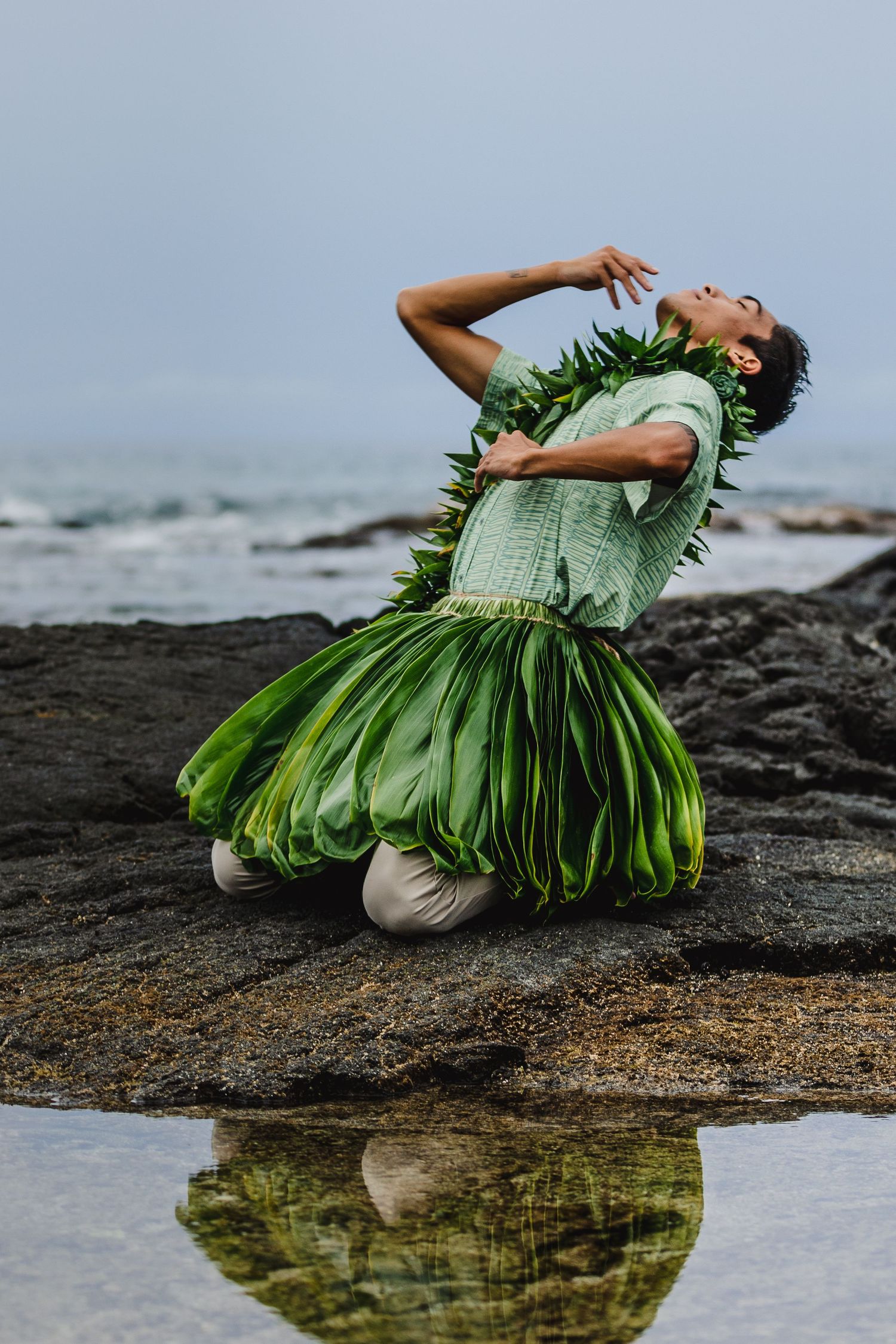 A figure in a flowing red dress poses dramatically on rocky coastline during golden sunset over ocean waves.