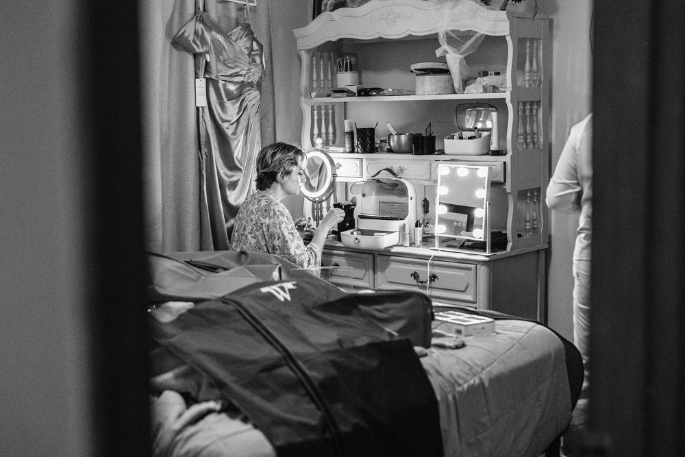 A black and white image showing the interior of a vintage bedroom with a dresser, mirror, and clothing items.