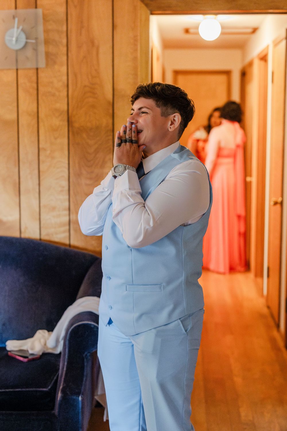 A person wearing a light blue suit expresses excitement in a hallway with warm lighting.