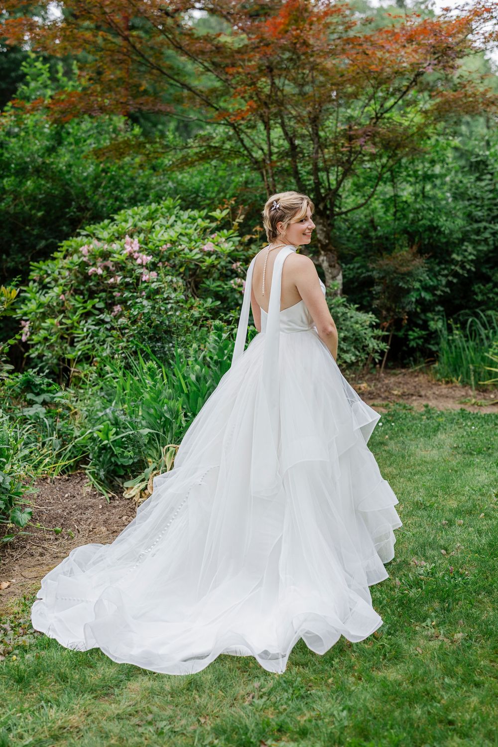 A bride in a flowing white wedding gown poses in a garden setting with autumn foliage in the background.