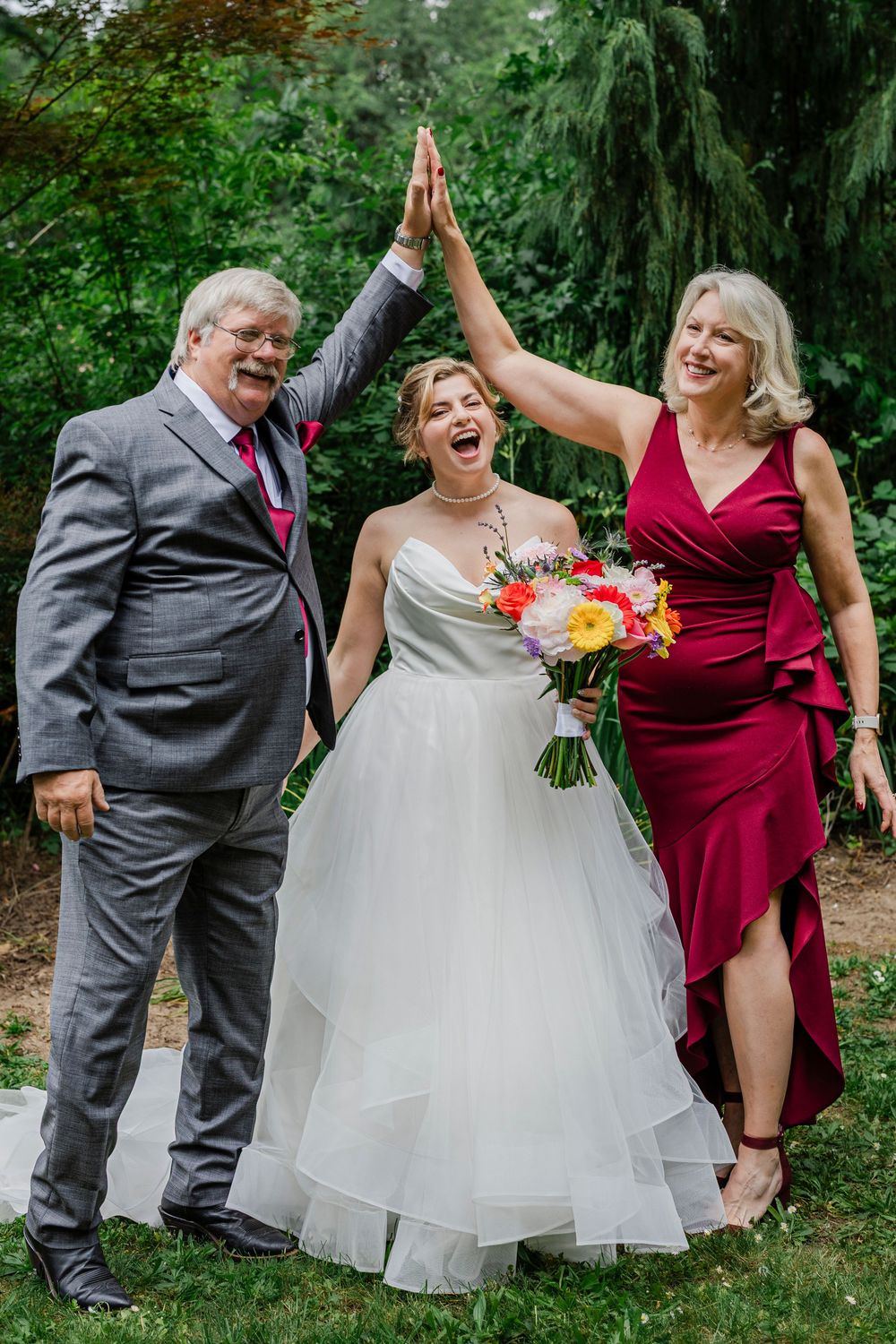 A wedding party celebrates with a high-five in a lush garden setting with colorful bouquet.