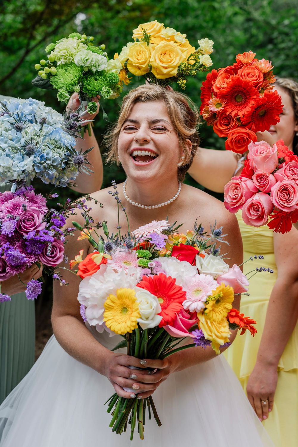 A joyful bride holding a vibrant multicolored bouquet surrounded by bridesmaids with colorful rose bouquets.