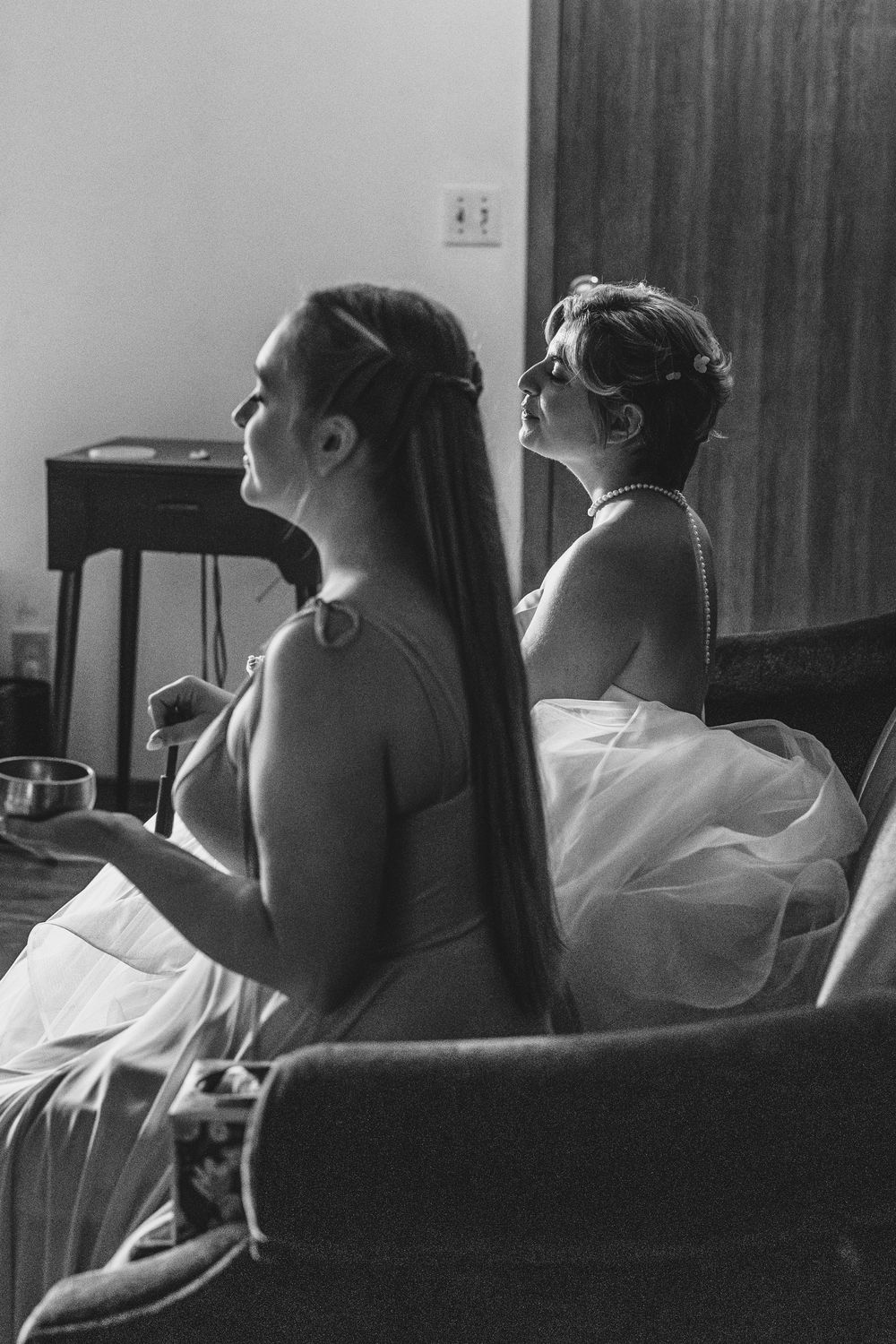 Black and white photo capturing intimate wedding preparation moments with bridesmaids getting ready on a couch.