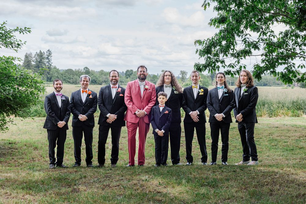 Wedding party poses outdoors with one member wearing a standout red suit among dark suits.