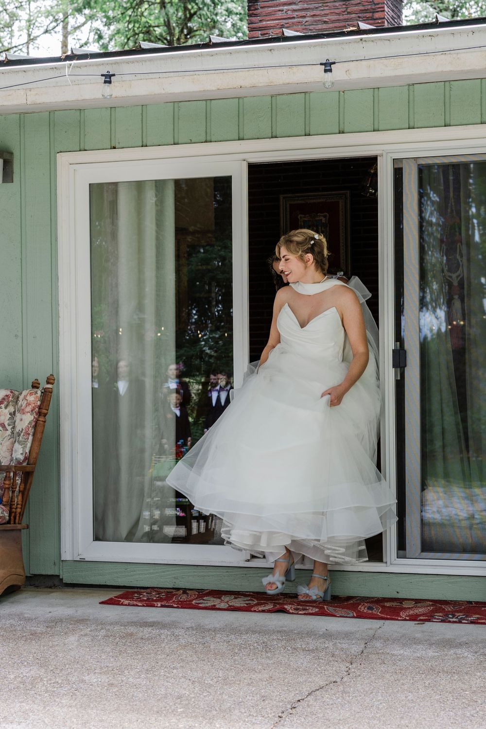 Bride in flowing white wedding dress twirls in front of mint green building with sliding glass doors.