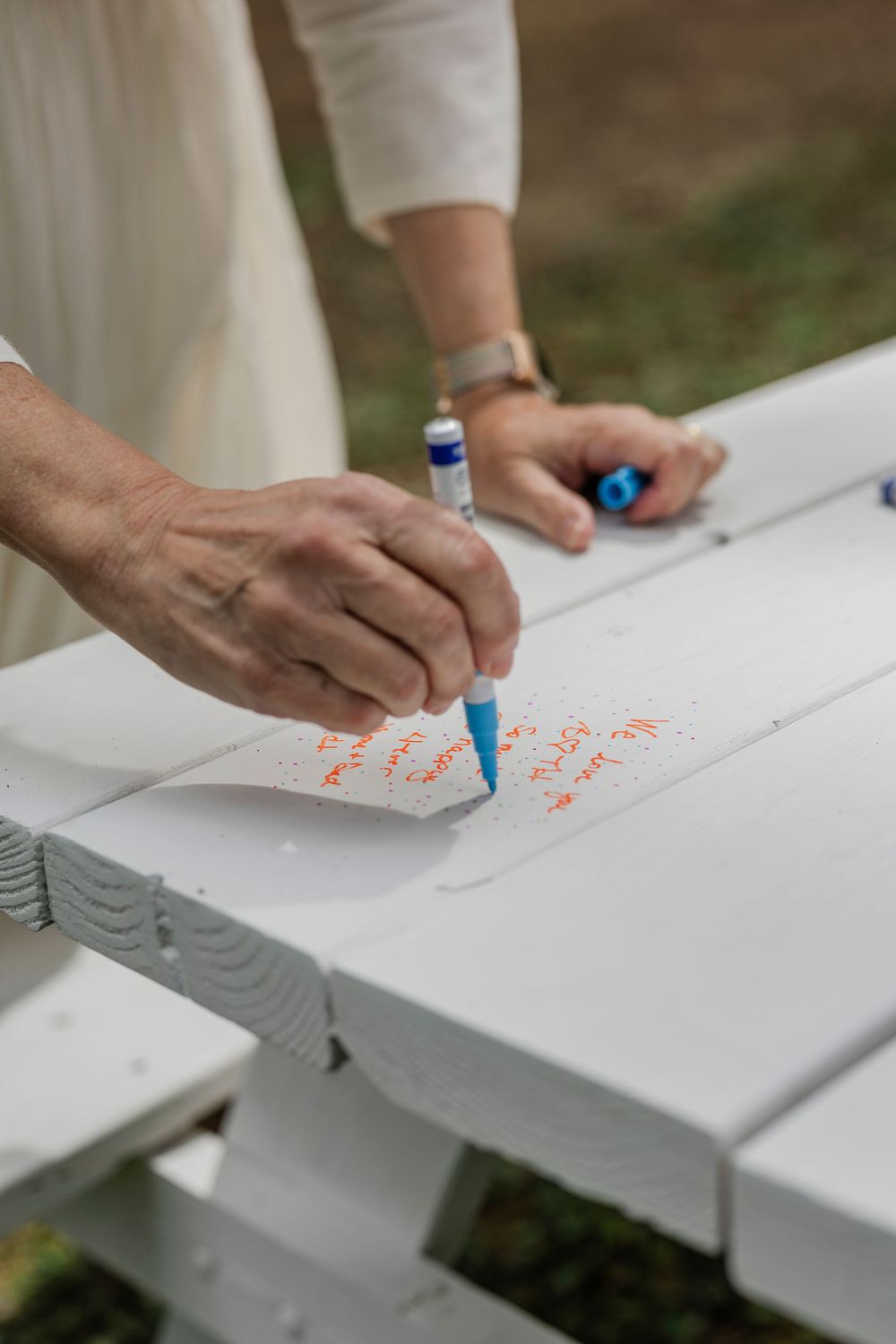 Hands writing on a white wooden surface during a wedding celebration.