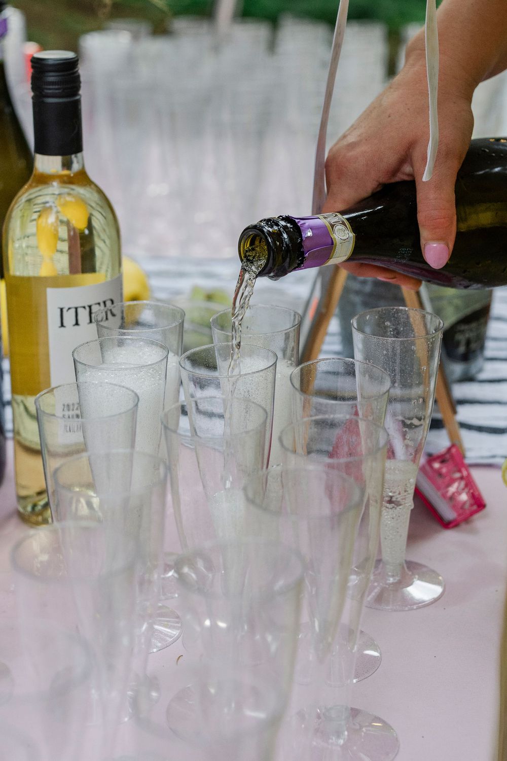 Wine being poured into champagne flutes at an outdoor reception table.