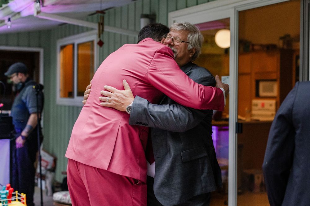 Two people share an emotional embrace at an outdoor wedding reception.