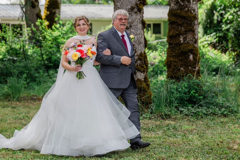 A bride carries a colorful bouquet while walking outdoors with an escort.