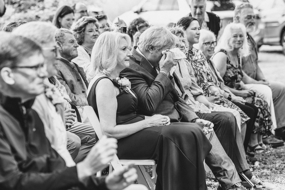 Black and white photo of wedding guests seated outdoors watching the ceremony.