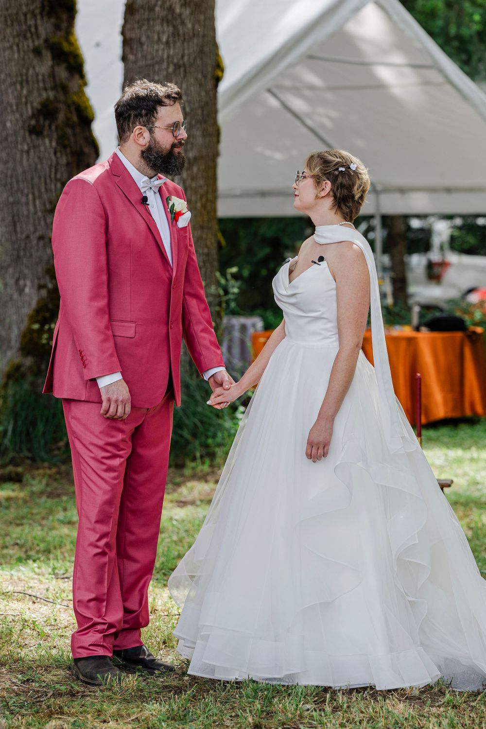 A couple shares a sweet moment at their outdoor wedding, with the groom in a pink suit and bride in a white ballgown.