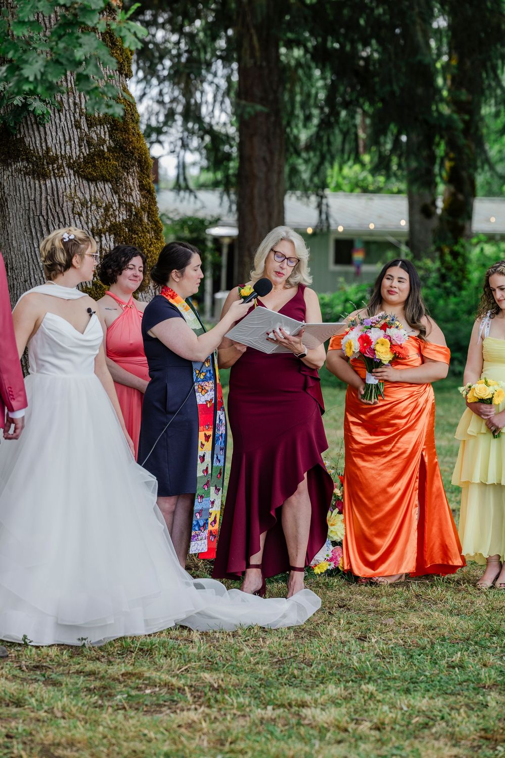 Wedding group sitting on chairs outdoors wearing burgundy, orange, and white dresses for a creative photo shoot.