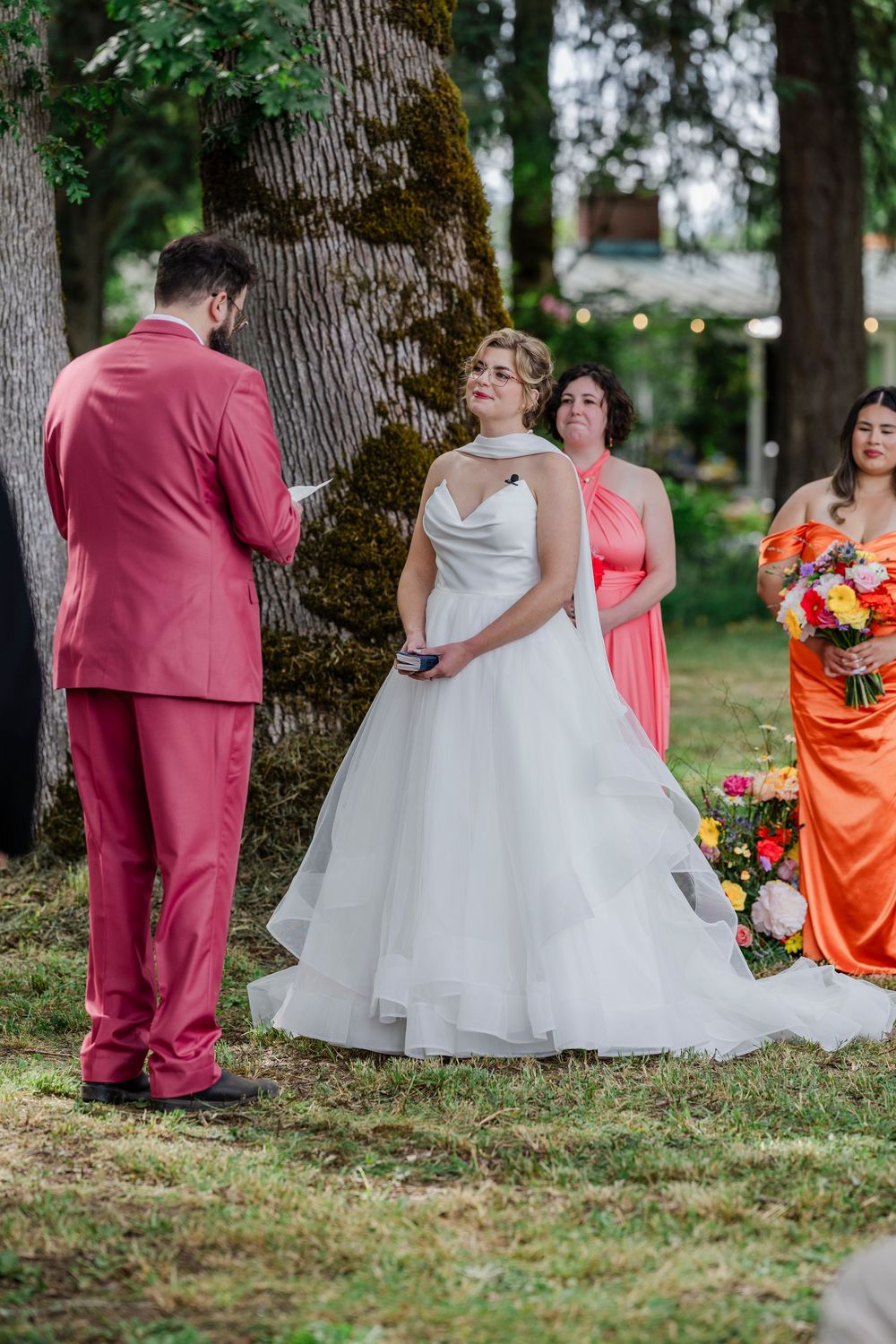 Wedding ceremony outdoors under mossy trees with the couple and wedding party in pink and orange dresses.