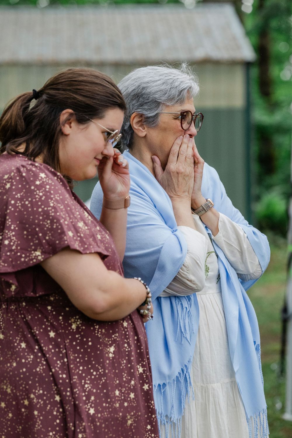 Three women standing together share an emotional moment outdoors, expressing grief or sadness.