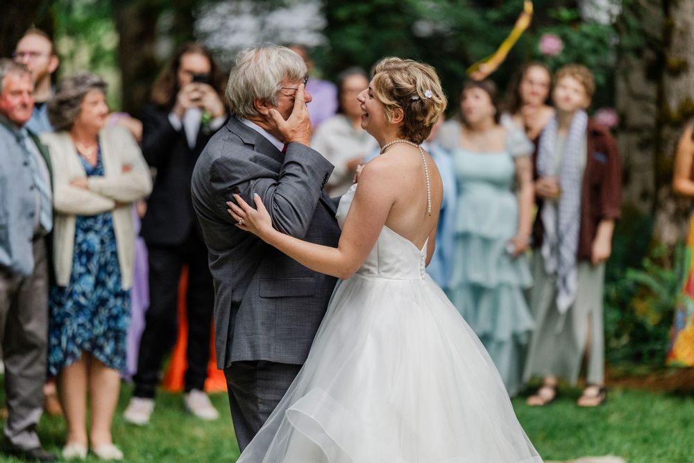 Two people dance at an outdoor wedding reception while guests watch from the sidelines in formal attire.