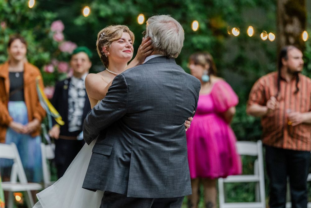 Couple shares romantic dance outdoors at garden wedding reception with string lights and guests in background.