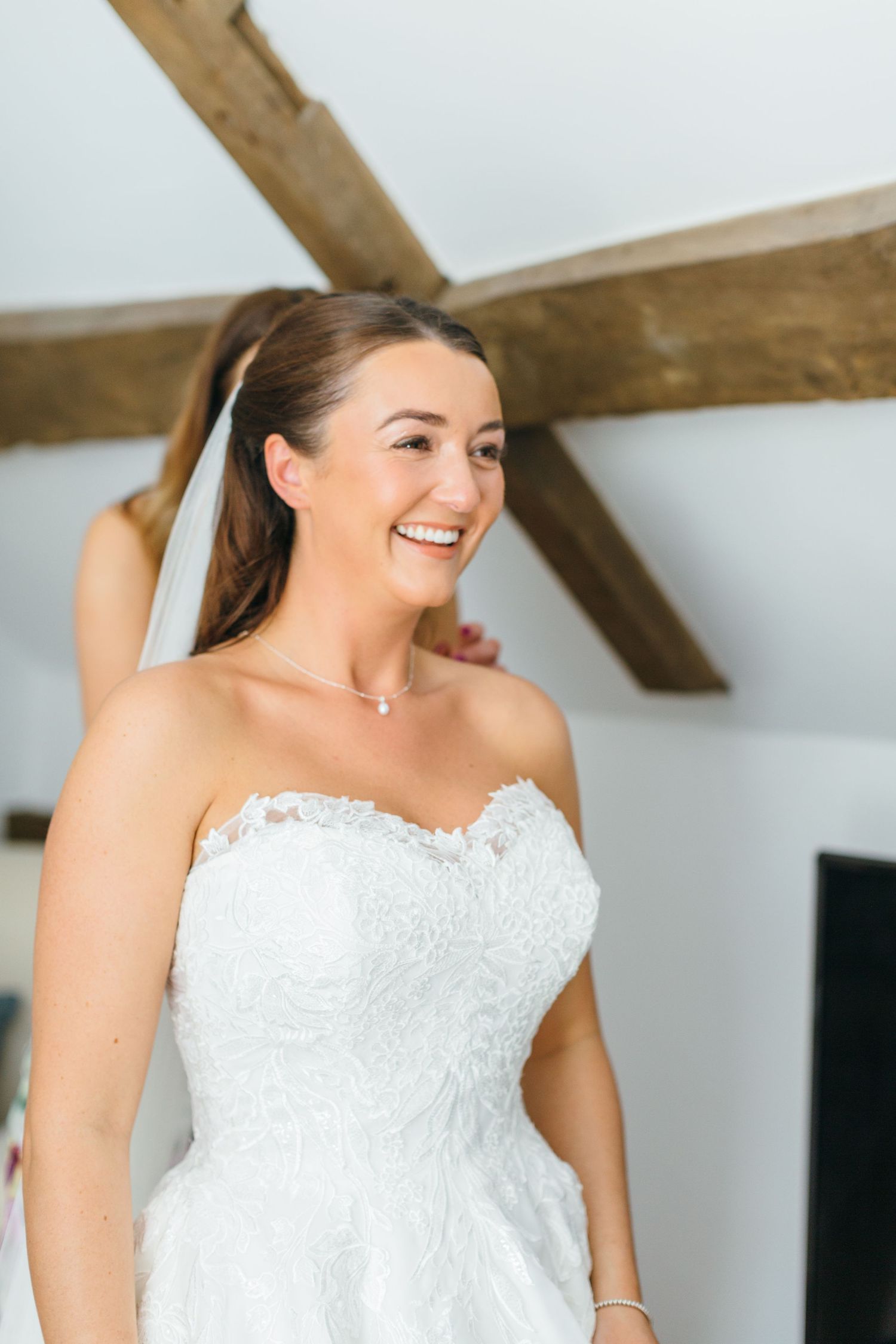 A bride wearing a strapless lace wedding gown with sweetheart neckline smiles joyfully under exposed wooden beams Lapstone Barn Wedding
