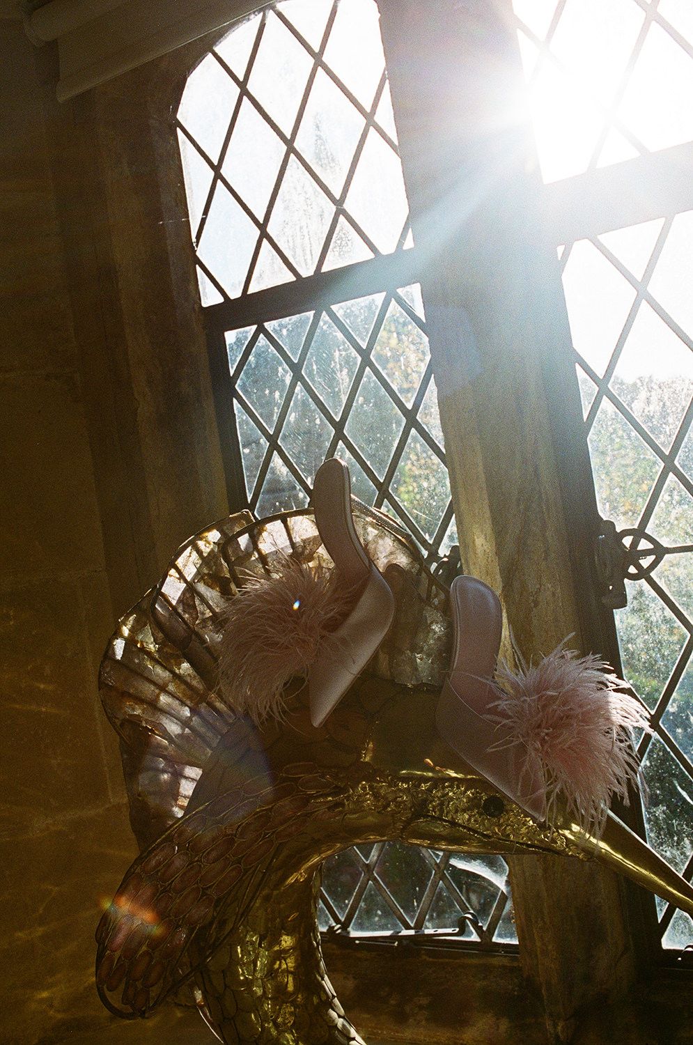 Sunlight streams through diamond pane windows onto a decorative wrought iron chandelier adorned with floral elements.