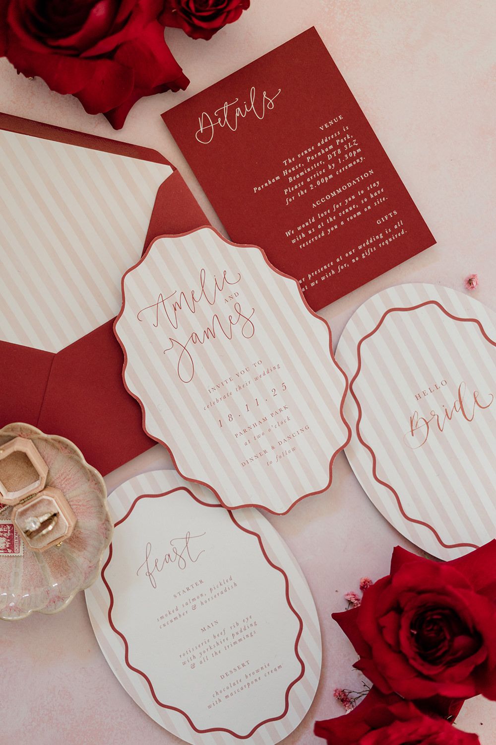 Elegant red and white scalloped wedding invitation suite with red roses and perfume bottle on light background.