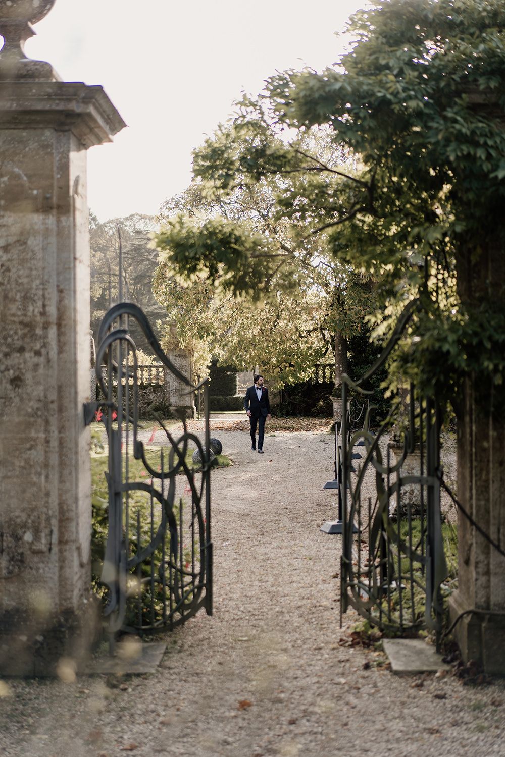 A romantic stone gate entrance with decorative wrought iron details opens up to a garden path in late afternoon light.