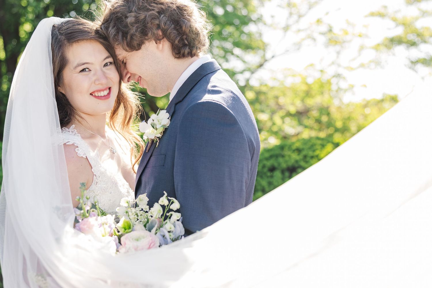 A gentle outdoor wedding moment captured with beautiful natural sunlight and white floral bouquet details.